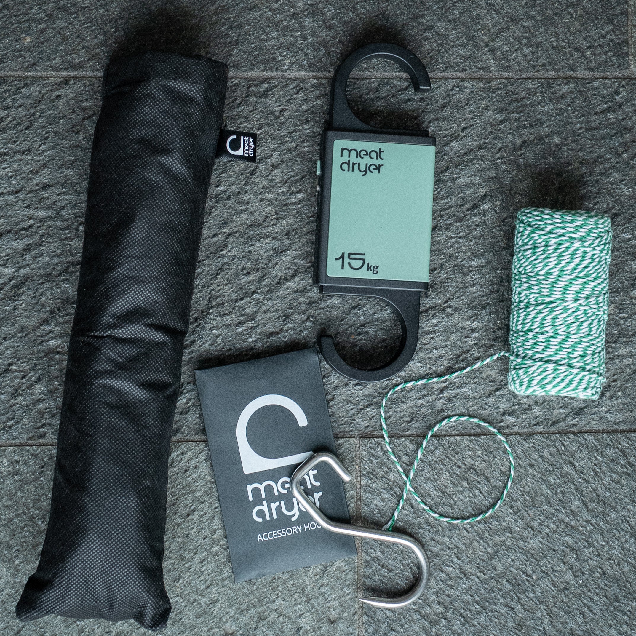 Meat drying equipment including a black insect net, string, and sharp metal meat hook on a stone surface