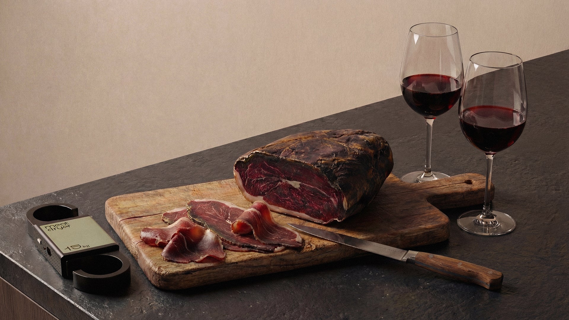 Wooden cutting board with sliced cured meat, a smart meat hook, and two glasses of red wine on a dark surface.